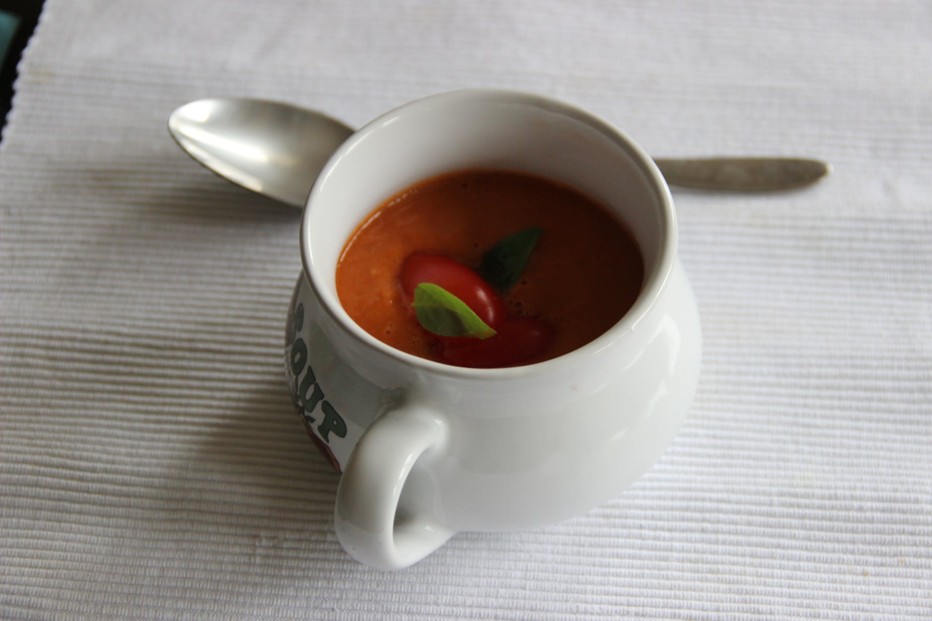 white ceramic mug with soup beside spoon